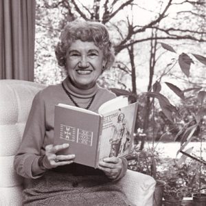 older white woman sitting on chair poses with open book