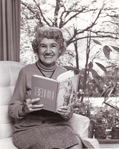older white woman sitting on chair poses with open book