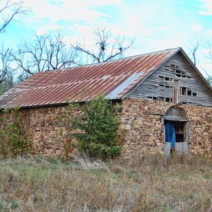 Abandoned barn with stone walls and rusted roof in overgrown field