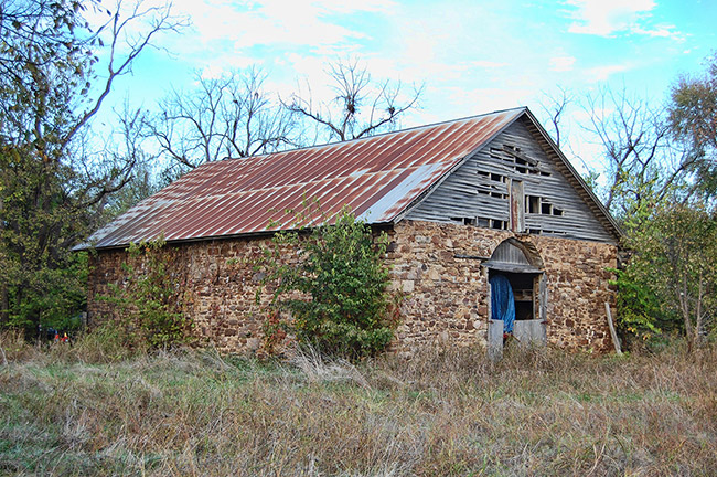 Abandoned barn with stone walls and rusted roof in overgrown field