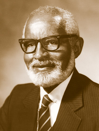 Older African-American man with glasses and beard smiling in suit and tie