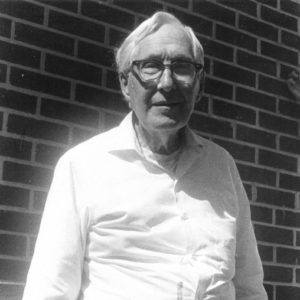 Portrait of white man in oxford shirt and glasses by brick wall
