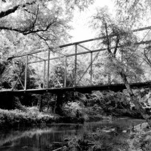 Rectangular frame steel bridge over creek in dense forest