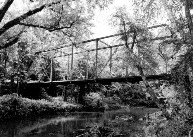 Rectangular frame steel bridge over creek in dense forest