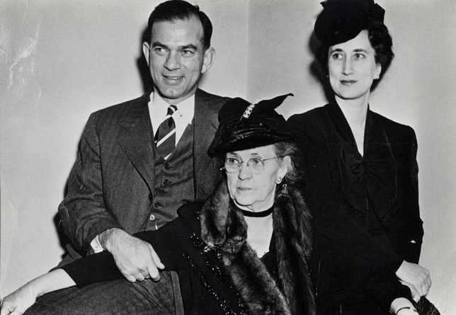 One white man two women in formal wear sit closely together man's hand on woman's arm