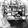 Old white man in glasses posing at his desk with typewriter and rotary telephone