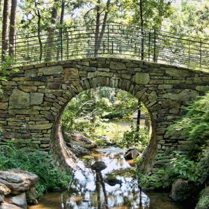 Stone bridge with railing and round opening over creek