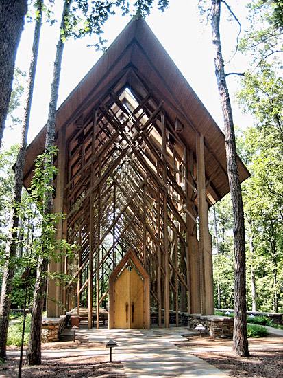 Narrow wood frame building with A-frame roof and hanging glass walls in wooded area