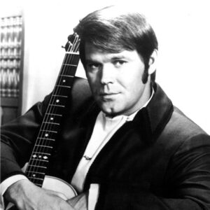 White man in suit posing with his arms around an acoustic guitar