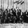 Group photo showing two rows of thirteen black men in tuxedos with instruments on stage with handwriting and arrow pointing to "William Grant Still"