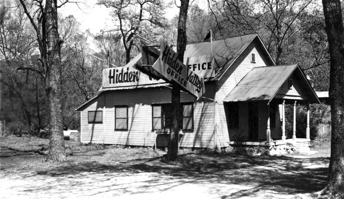 Wood frame house in woods with signs reading "Hidden Valley Office"