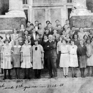 Group photo white school children and male teacher outside brick school with columns