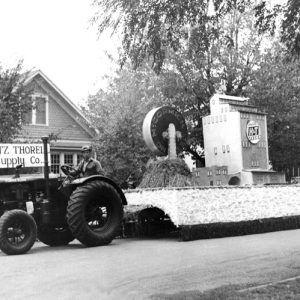 White man on tractor pulling factory parade float in front of house