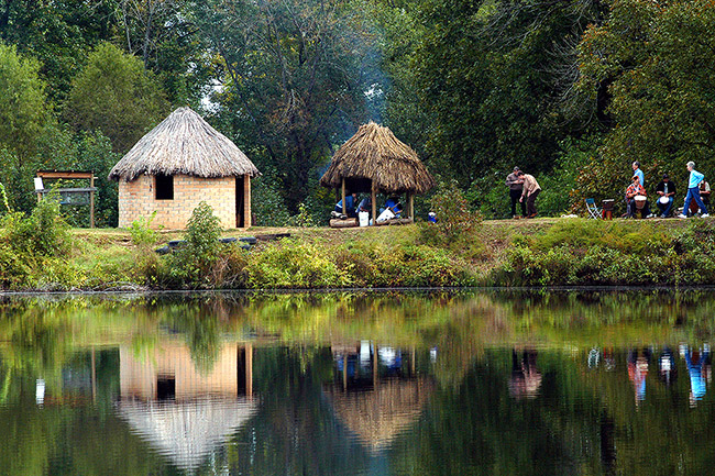 White visitors with grass pavilion and round hut on lake
