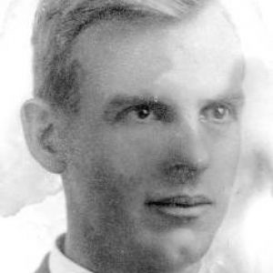 Portrait photo of a young white man with a slight smile beaming eyes short parted hair wearing a suit jacket and tie