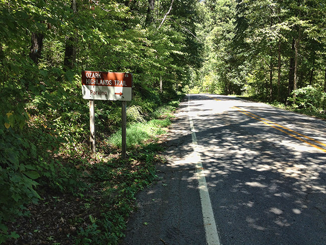 "Ozark Highlands Trail parking" sign with street and trees on both sides