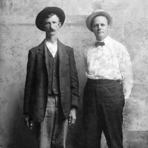 Portrait two white men in semiformal attire with hats, architectural photograph backdrop