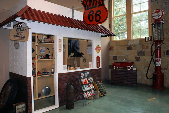 Model store front with shelves of various items and sign reading "Phillips 66"