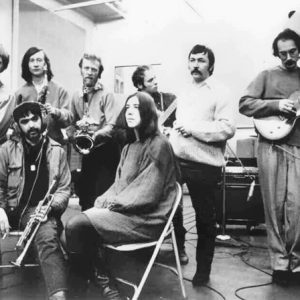 five people with instruments and two without standing and sitting in studio