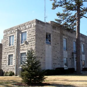 two story gray stone building with large pine tree in front