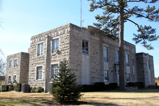 two story gray stone building with large pine tree in front