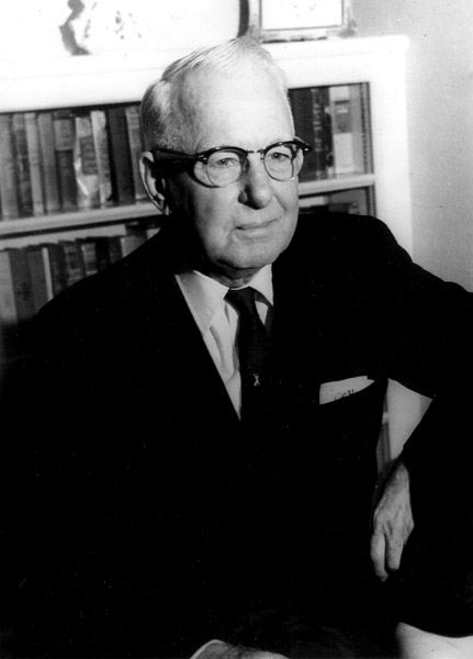 white man in glasses wearing suit in front of bookcases