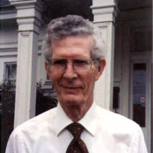 Old white man with glasses smiling in shirt and tie with pens in pocket protector