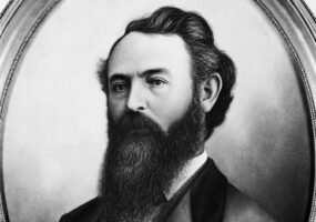 oval-framed portrait of a white man with dark hair and a long beard wearing a suit