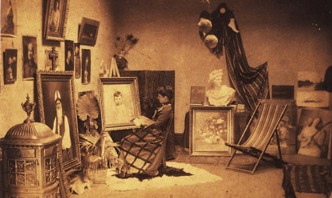 woman sitting in art studio surrounded by several paintings