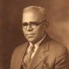 Portrait photo of a black man with short hair and glasses wearing a coat vest and tie and a pocket square