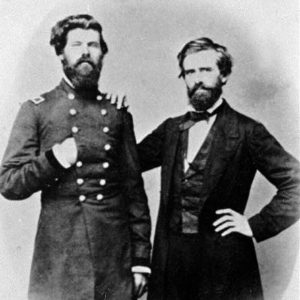 Portrait photo of a bearded white man in military uniform with another white man in a suit and bow tie with his hand on the military man's shoulder