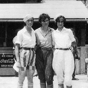 Three young white women with short hair standing with their arms around each other's backs