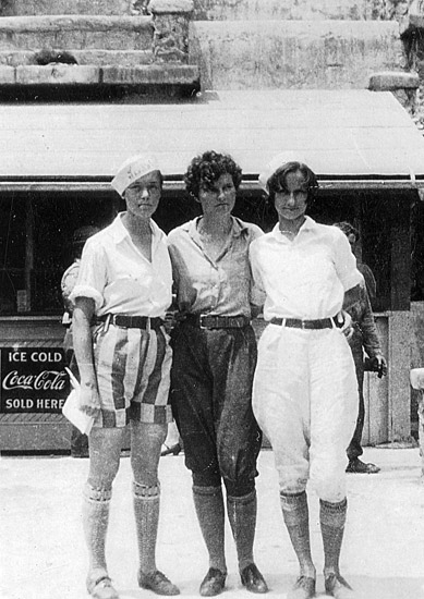 Three young white women with short hair standing with their arms around each other's backs