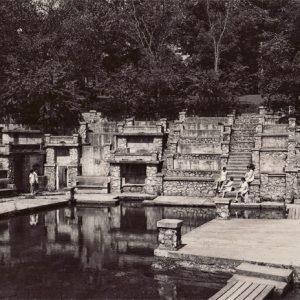 Young white women sitting on steps of concrete and stone amphitheater on lake with trees in the background