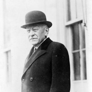 white man in bowler hat and coat standing outside
