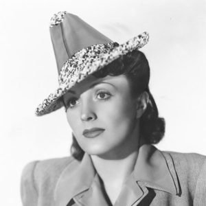White woman with neck length hair wearing pointed hat and coat