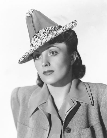 White woman with neck length hair wearing pointed hat and coat