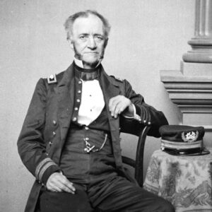 white man in military regalia sitting in chair with hat on table beside him