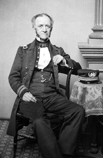 white man in military regalia sitting in chair with hat on table beside him