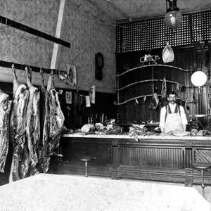 two white men in butcher shop with hanging meat