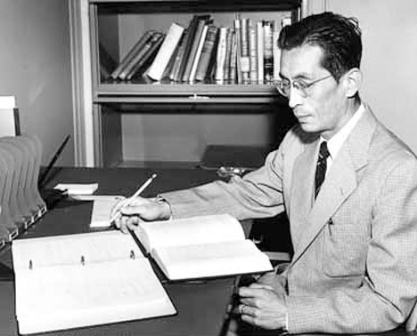 Japanese-American man in suit and tie reading at his desk