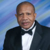 African-American man with mustache smiling in tuxedo
