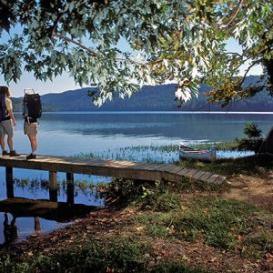 Two white people standing on a wooden boat dock on large lake surrounded by mountains