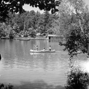 three girls canoeing on lake surrounded by trees with boat dock in distance