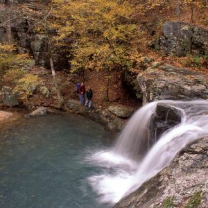 two hikers next to waterfall amid fall foliage