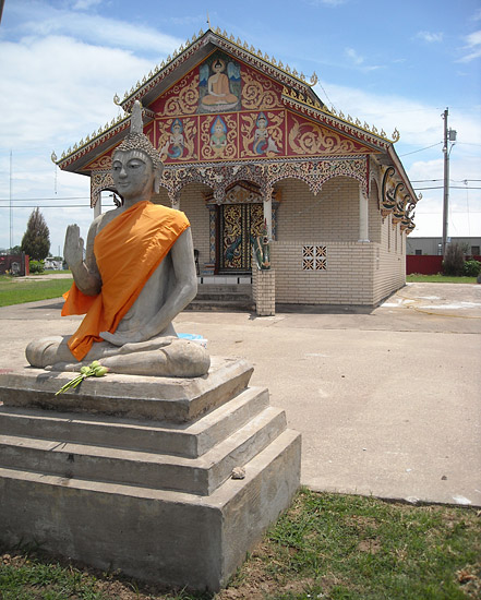 Single-story brick temple building with statue of Buddha on pedestal in the foreground