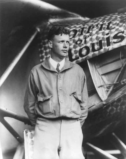 Young white man in suit and jacket standing beside his airplane named the "Spirit of St. Louis"