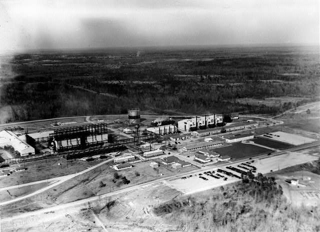 Aerial view of an industrial complex with various buildings and machinery with roads plains and horizon in background
