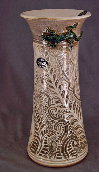 Green lizard on tan vase with plant etchings and small oval sticker