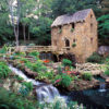 Narrow stone building with water wheel and foot bridges with wooden railings and waterfall in the foreground